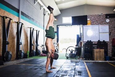 Männlicher Sportler ohne Hemd übt Handstand auf dem Boden im Fitnessstudio - MIMFF00420