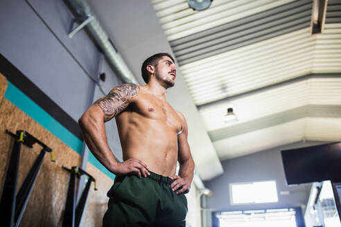 Hemdloser junger Mann mit verschränkten Armen im Fitnessstudio - MIMFF00421