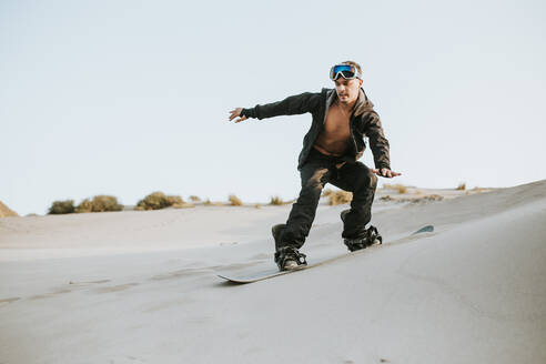 Young man sand surfing on sand dunes against clear sky at Almeria, Tabernas desert, Spain - MIMFF00434