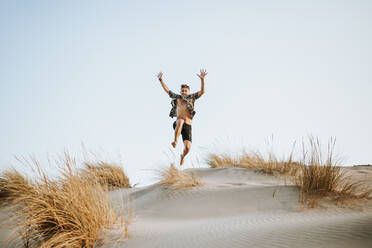 Cheerful young man jumping over sand at Almeria, Tabernas desert, Spain - MIMFF00440