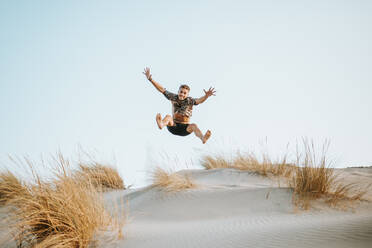 Smiling young man jumping in desert against clear sky at Almeria, Tabernas desert, Spain - MIMFF00441