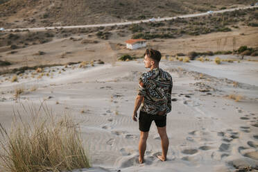 Junger Mann, der wegschaut, während er auf Sand in Almeria, Tabernas-Wüste, Spanien, steht - MIMFF00443