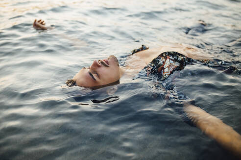 Young man with eyes closed wearing unbuttoned shirt while floating in water - MIMFF00457