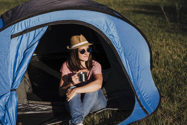 Beautiful woman wearing sunglasses with drink relaxing in tent - EBBF02191