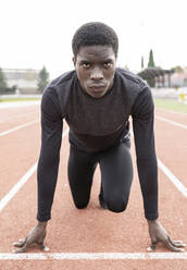 Confident sportsman in ready position to run on running track - JCCMF00872