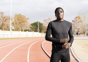 Young sportsman standing on running track during sunny day - JCCMF00883