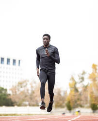 Young sportsman running with dedication on track against clear sky - JCCMF00891