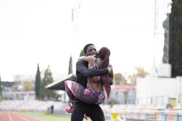 Junger Sportler trägt Sportlerin und umarmt auf der Strecke gegen den klaren Himmel - JCCMF00897