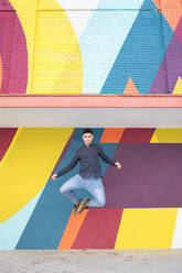 Young man jumping against colorful wall - IFRF00294