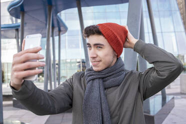 Junger Mann mit Strickmütze nimmt Selfie durch Handy in der Stadt - IFRF00312