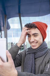 Smiling man with hand in hair taking selfie in city - IFRF00315