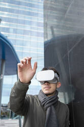 Young man gesturing while watching on VR box by black wall - IFRF00321