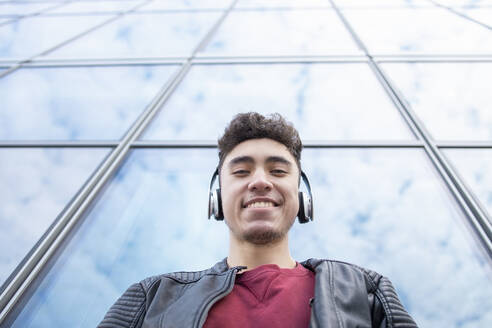 Glücklicher junger Mann hört Musik vor einem Glasgebäude - IFRF00327