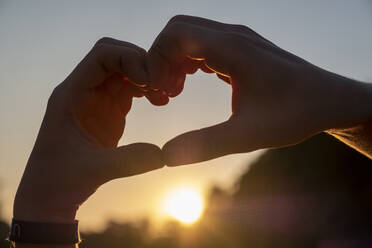 Man making heart shape with hands against sky during sunset - LBF03310