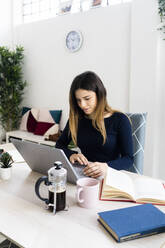 Young female student studying on laptop in living room - GIOF10609