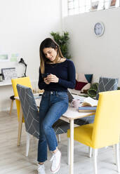 Junge Studentin, die zu Hause am Tisch sitzend mit ihrem Smartphone lernt - GIOF10618