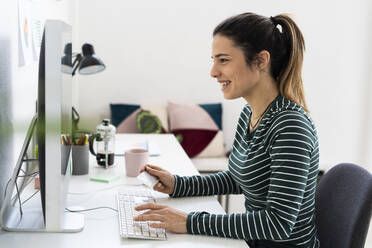 Happy female entrepreneur using computer while paying through credit card in office - GIOF10636