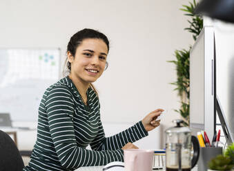 Kreative Geschäftsfrau, die eine Kreditkarte hält, während sie im Büro am Computer sitzt - GIOF10638