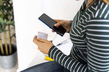 Berufstätige Frau mit Kreditkarte beim Online-Einkauf über ihr Smartphone am Arbeitsplatz - GIOF10639