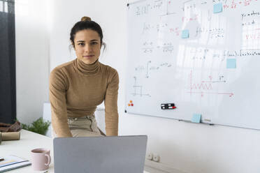 Studentin mit Laptop, die zu Hause am Whiteboard sitzt und lernt - GIOF10669