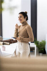 Happy young woman laughing while talking on mobile phone at home - GIOF10686