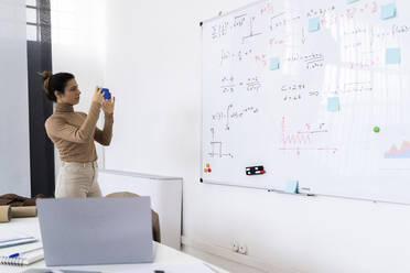 Female student taking photograph of math whiteboard while standing at home - GIOF10687