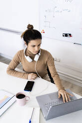 Female student with headphones using laptop while studying at home - GIOF10688