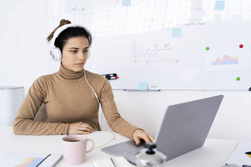 Junge Studentin beim E-Learning am Laptop über Kopfhörer zu Hause - GIOF10690