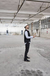 Male architect with map contemplating while looking up in constructing building - VEGF03540