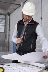 Male architect analyzing blueprint on table while standing in building at site - VEGF03550