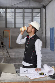 Männlicher Architekt trinkt Kaffee, während er an einem Tisch in einem Gebäude steht - VEGF03563