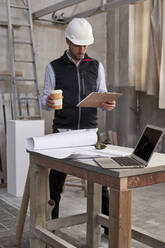 Männlicher Architekt mit Kaffee in der Hand bei der Analyse eines Plans in einem Gebäude - VEGF03564