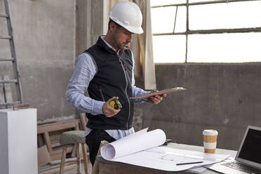 Male building contractor analyzing plan while standing at table in building - VEGF03565