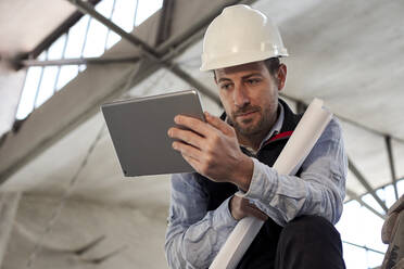 Männlicher Ingenieur arbeitet über einem digitalen Tablet, während er in einem Gebäude auf der Baustelle steht - VEGF03582