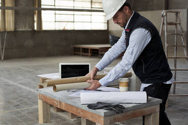 Male architect placing blueprints on table in building at construction site - VEGF03588