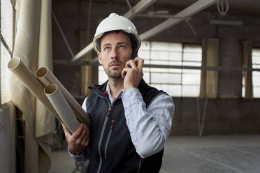 Männlicher Immobilienentwickler, der über ein Mobiltelefon spricht, während er in einem Gebäude steht - VEGF03592