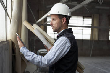 Male real estate developer holding blueprint using digital tablet while standing in building - VEGF03594