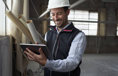 Lächelnder Bauunternehmer, der auf einer Baustelle steht und ein digitales Tablet benutzt - VEGF03595