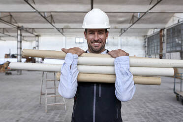 Smiling male architect holding cardboards while standing in building - VEGF03606