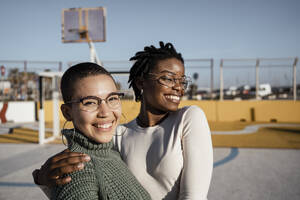 Junge Frauen, die lächelnd auf dem Basketballplatz stehen - RCPF00553