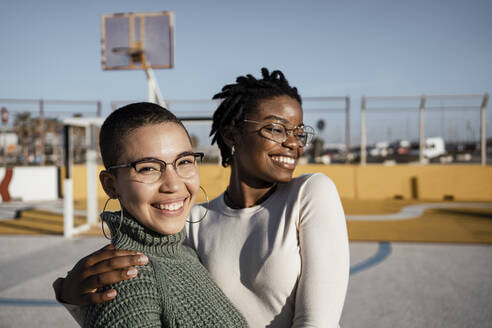 Young women smiling while standing at basketball court - RCPF00553