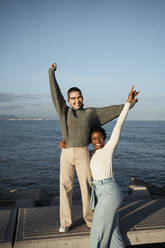 Carefree friends standing with hand raised against sky - RCPF00573