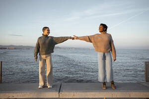 Freund streckt die Hände aus, während er auf einer Bank in der Ferne am Meer steht - RCPF00602