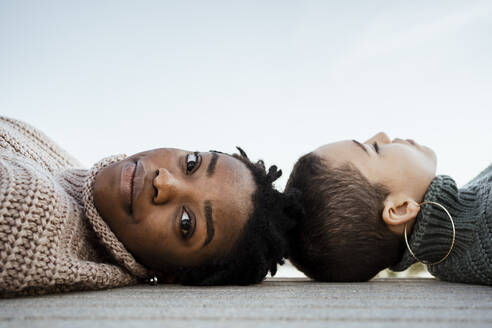 Woman staring while resting with friend on bench against sky - RCPF00606