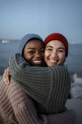 Glückliche junge Frauen, die sich gegenseitig umarmen, während sie gegen den Himmel stehen - RCPF00623
