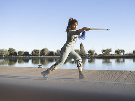 Weibliche Athletin übt Kampfsport mit Schwert am See gegen den klaren Himmel - JCCMF00901