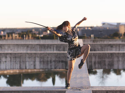 Weibliche Athletin übt Schwert auf Struktur gegen klaren Himmel bei Sonnenuntergang - JCCMF00924