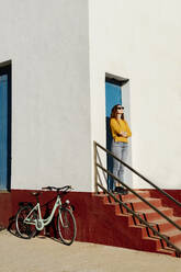 Young woman with arms crossed standing on staircase corrugated iron during sunny day - AFVF08058