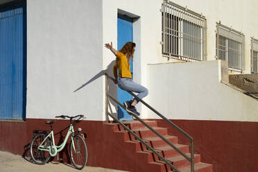 Junge Frau rutscht auf dem Geländer von weißen gebaut Struktur während sonnigen Tag - AFVF08059