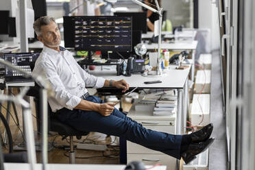 Thoughtful entrepreneur with digital tablet looking away while sitting at office - PESF02458